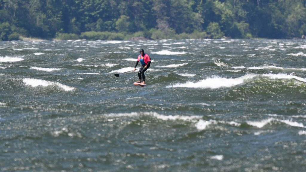 A photo of a SUP foil rider on a downwind run in the Columbia Gorge near the Hatchery